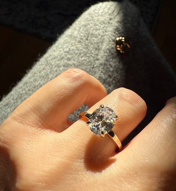 Ovaler Solitär-Diamantring in 18K Gelbgold – funkelnder natürlicher Diamant im Sonnenlicht, aufgenommen von CAREDIAMONDS.